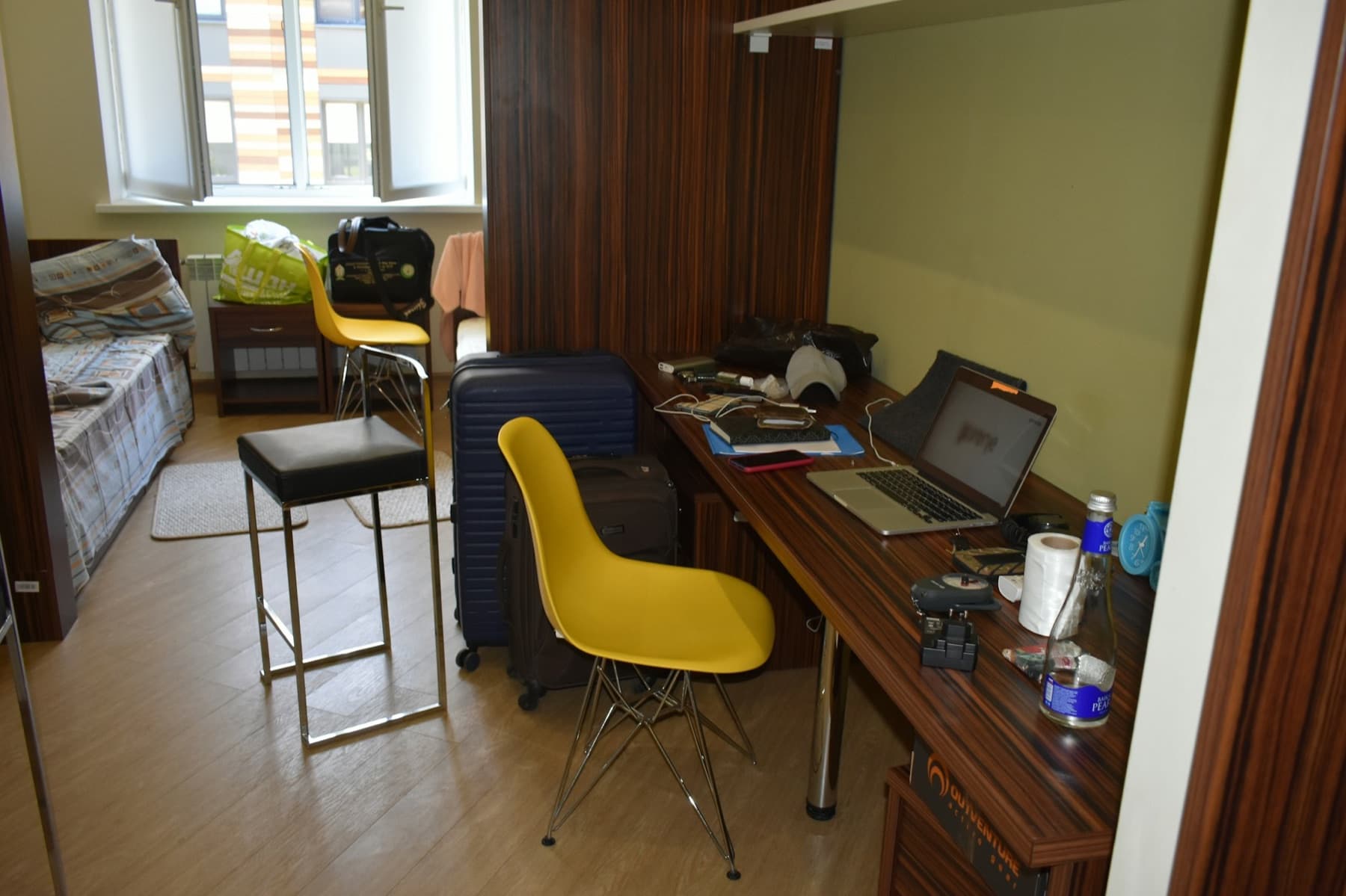 A dorm room with a desk, a yellow chair and a laptop