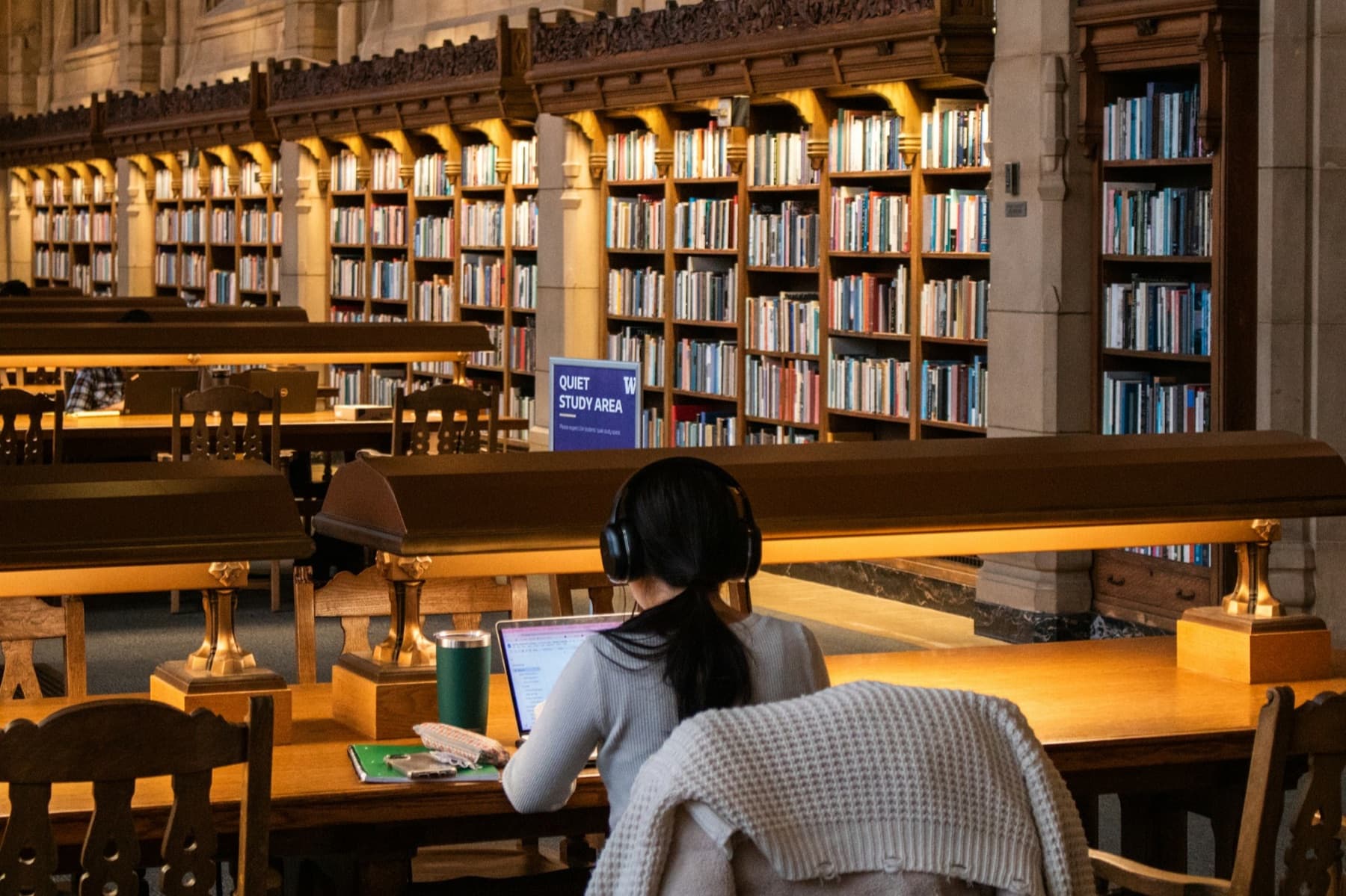 A student in headphones working on a laptop in a wood-panelled library