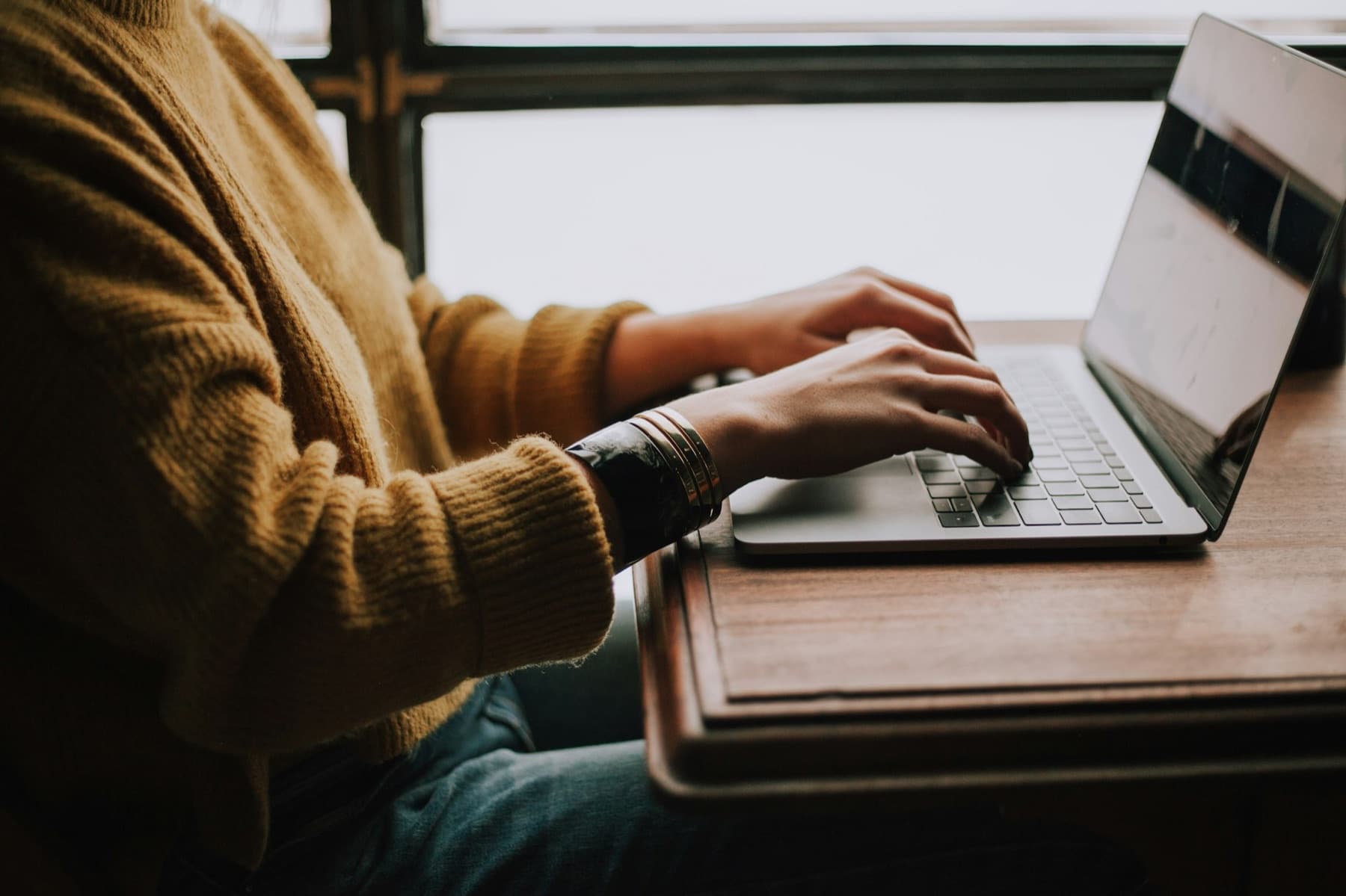 Hands in a mustard sweater typing on a laptop