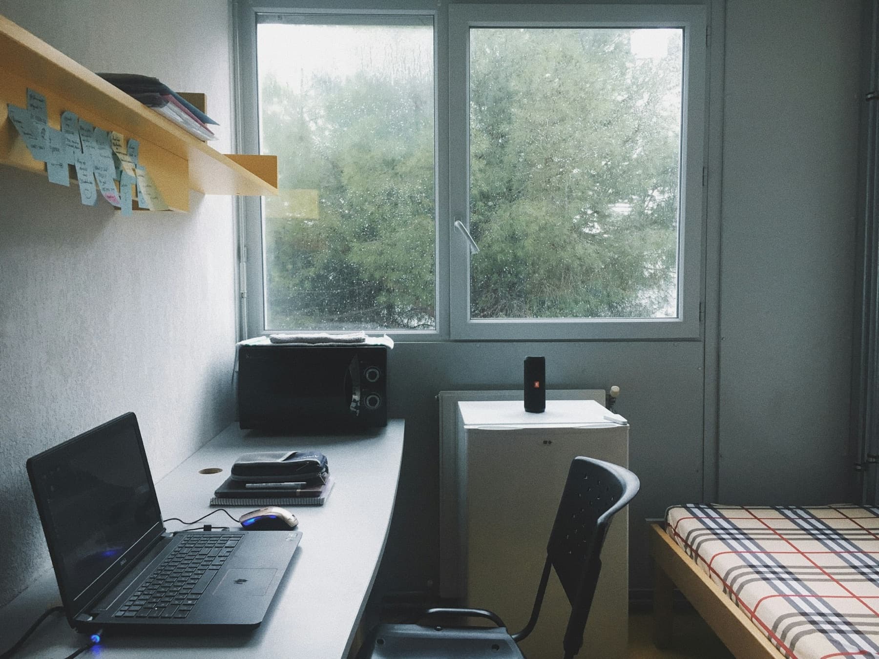 A small dorm desk with a laptop under a window