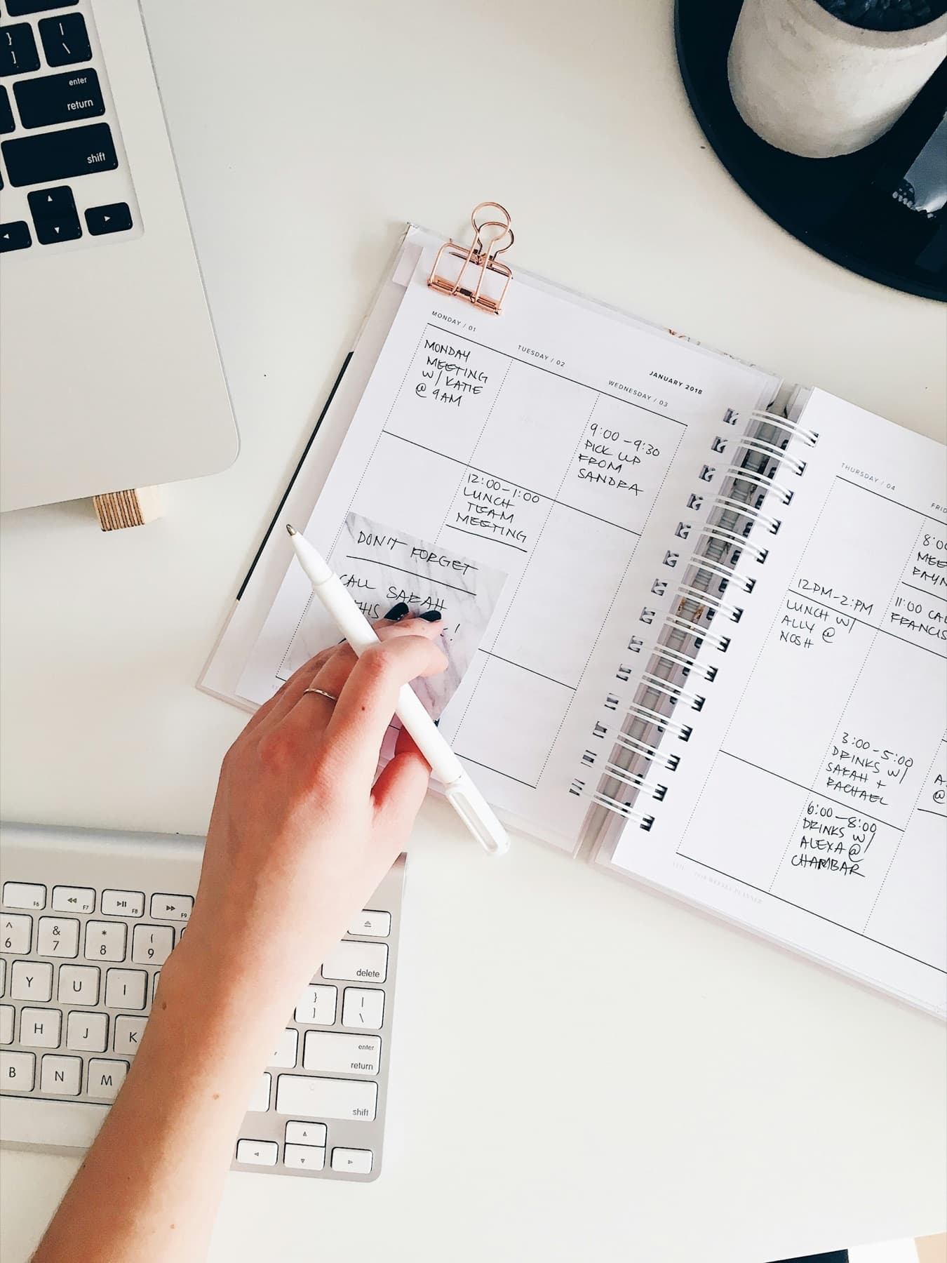 A hand writing in a spiral planner next to a keyboard